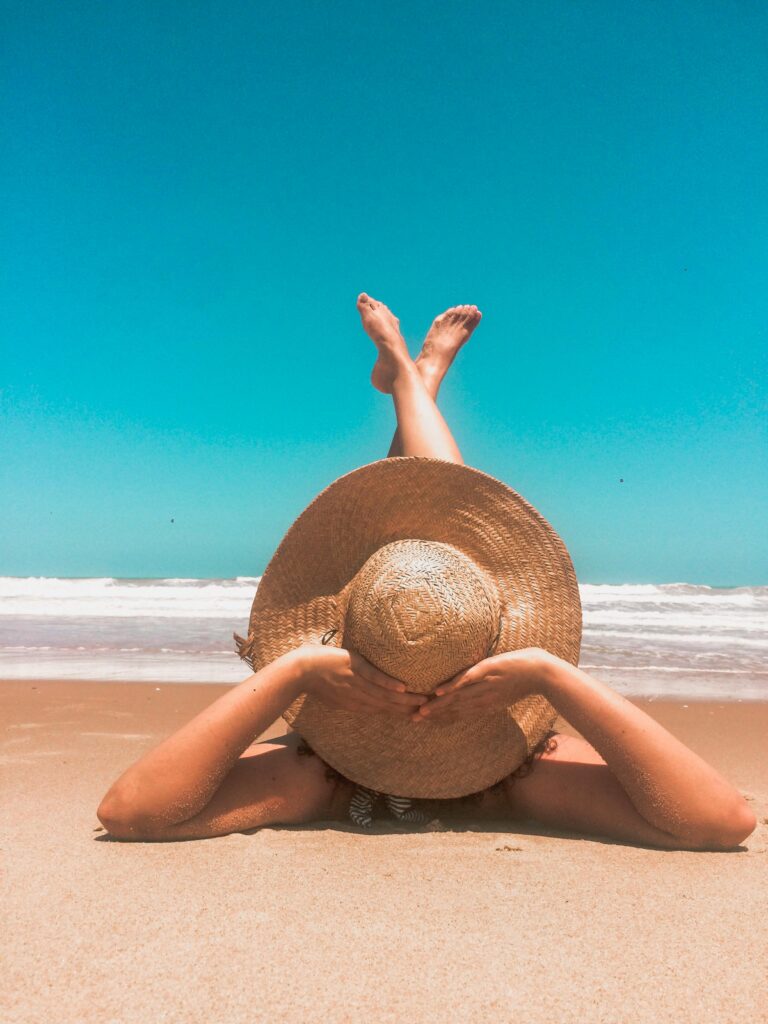 Femme sur la plage à bronzer au soleil avec un chapeau de paille.